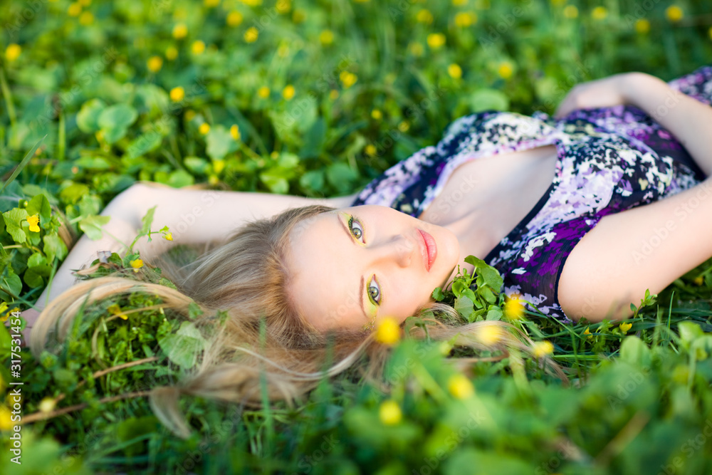 Portrait of young beautiful blond woman lying in grass and flowers on summer day with green nature landscape Portrait of young beautiful blond woman lying in grass and flowers on summer day with green nature landscape