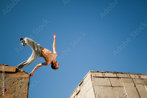 Young man jumping and practicing parkour between two building outside on clear summer day