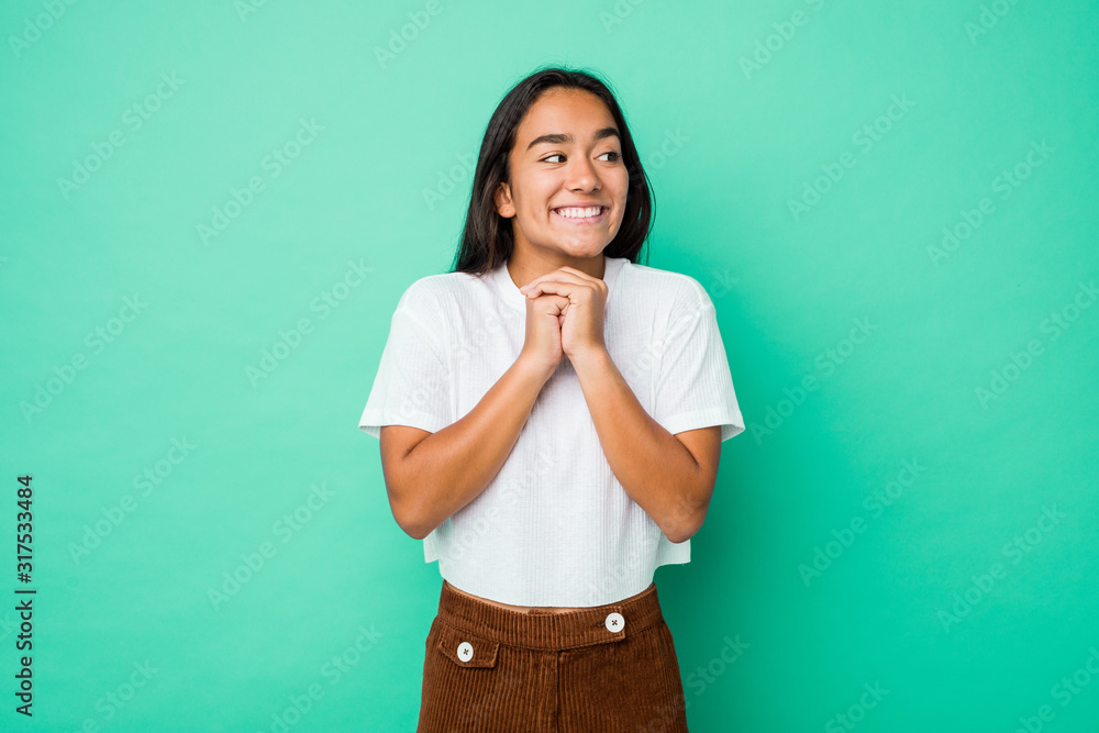 Young mixed race indian woman isolated keeps hands under chin, is looking happily aside.
