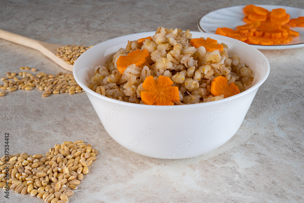 Fototapeta premium Spelt porridge in a white bowl and decorated with an asterisk carrot, diet food.