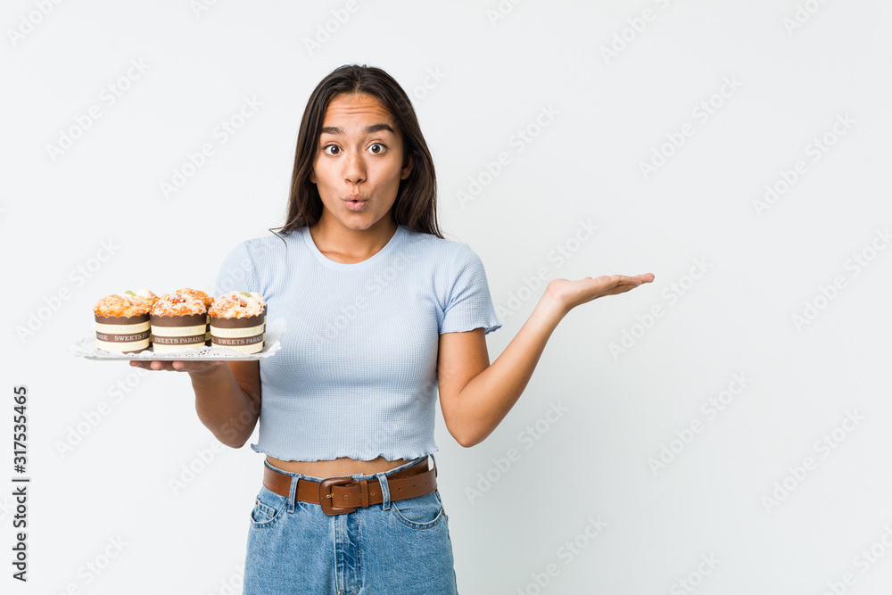 Young mixed race indian holding a sweet cakes impressed holding copy space on palm. Young mixed race indian holding a sweet cakes impressed holding copy space on palm.