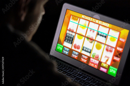 Canvas Print Gambling addicted man with glasses in front of online casino slot machine on laptop computer at night - loosing his money