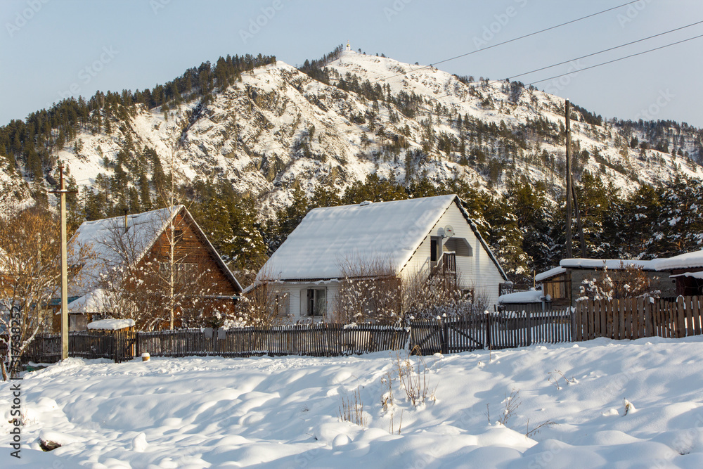 Wooden houses covered with snow at the foot of the mountains in winter
