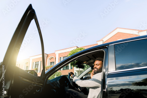 Foto African American male boss businessman using smartphone for making call during while sitting in luxury car with open door, serious man concentrated phoning to partner