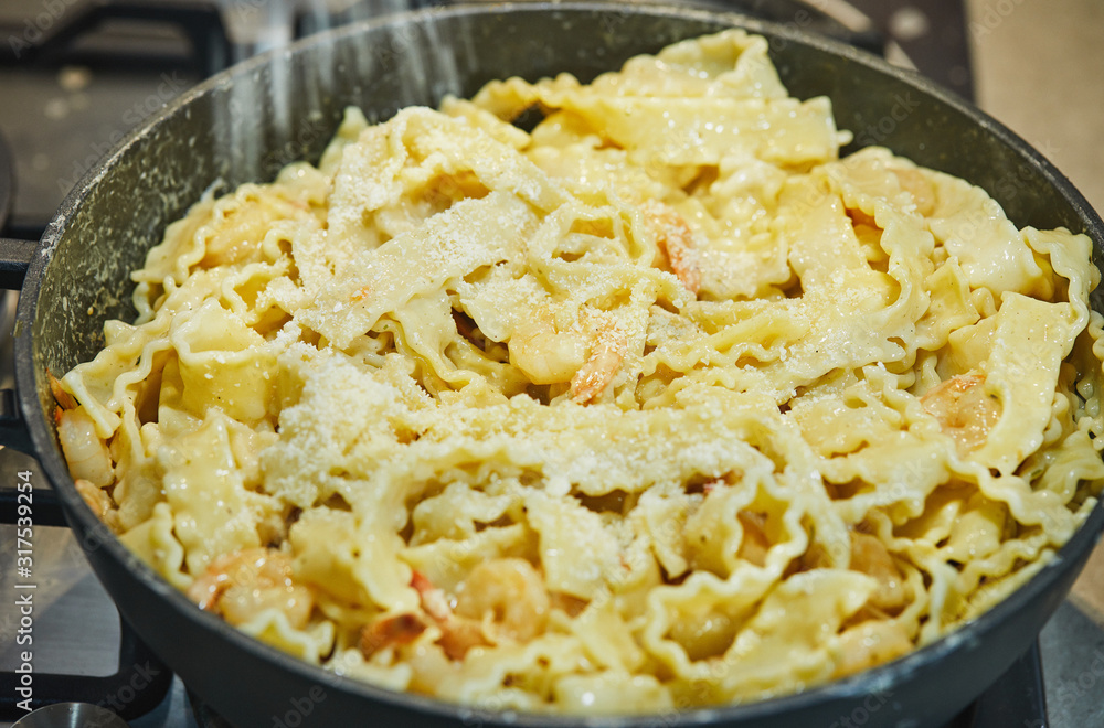 Fried shrimp with Italian pasta called mafaldine in a pan sprinkled with parmesan Fried shrimp with Italian pasta called mafaldine in a pan sprinkled with parmesan