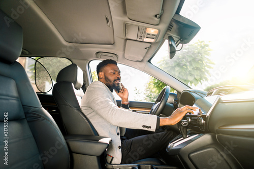 African businessman talking on mobile phone inside a car and touching the tablet. Young entrepreneur working during travelling to office in a luxury car.