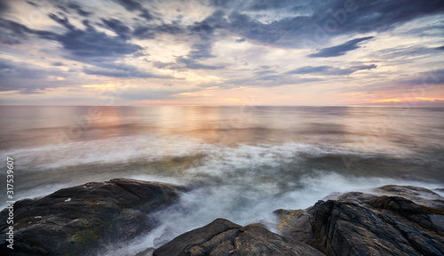 Scenic sunset over water seen from rocky shore, long exposure picture.
