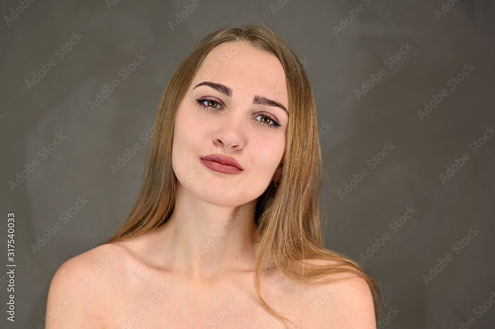 Naklejka premium Horizontal beauty photo of a pretty girl with long hair and great makeup and good skin. Universal concept female portrait on a gray background.