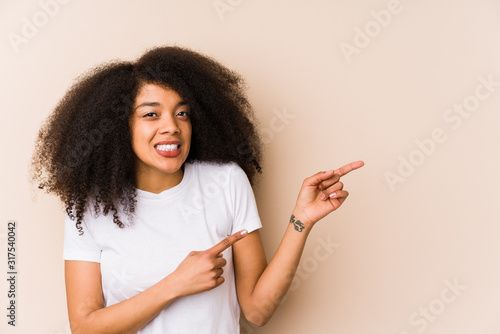 Young african american woman shocked pointing with index fingers to a copy space.