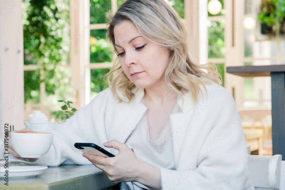 Cute blonde girl sitting in a cafe with a Cup of coffee with a mobile device, spending time on social networks Cute blonde girl sitting in a cafe with a Cup of coffee with a mobile device, spending time on social networks
