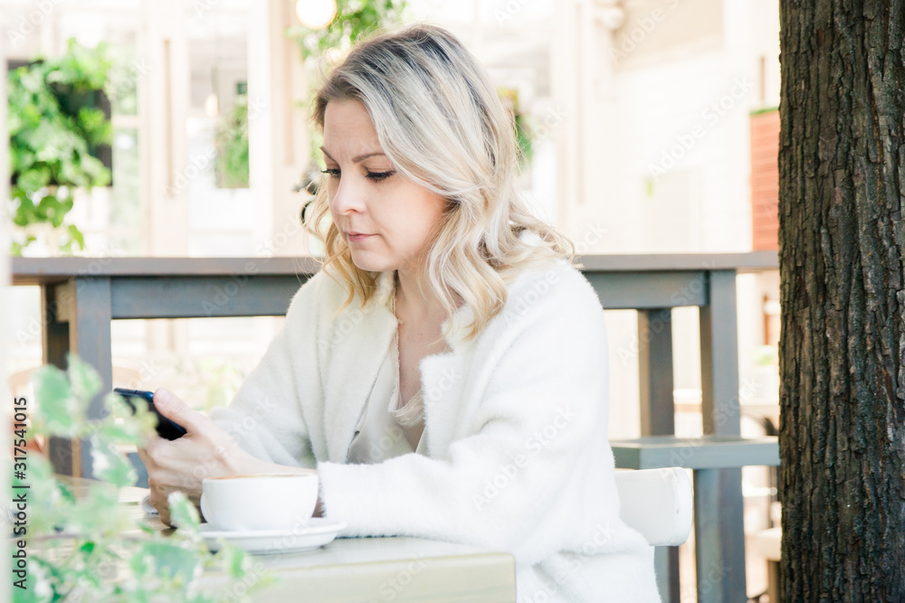 Cute blonde girl sitting in a cafe with a Cup of coffee with a mobile device, spending time on social networks Cute blonde girl sitting in a cafe with a Cup of coffee with a mobile device, spending time on social networks