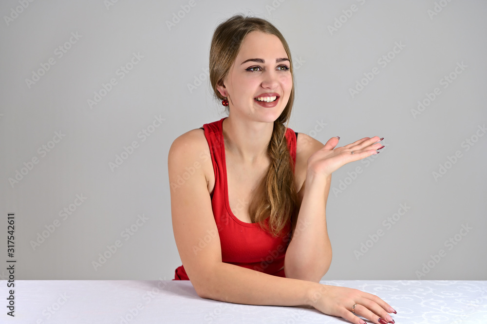 Universal concept female portrait on a white background. Horizontal photo of a pretty smiling girl with long hair and great makeup sitting at a white table in the studio. Universal concept female portrait on a white background. Horizontal photo of a pretty smiling girl with long hair and great makeup sitting at a white table in the studio.