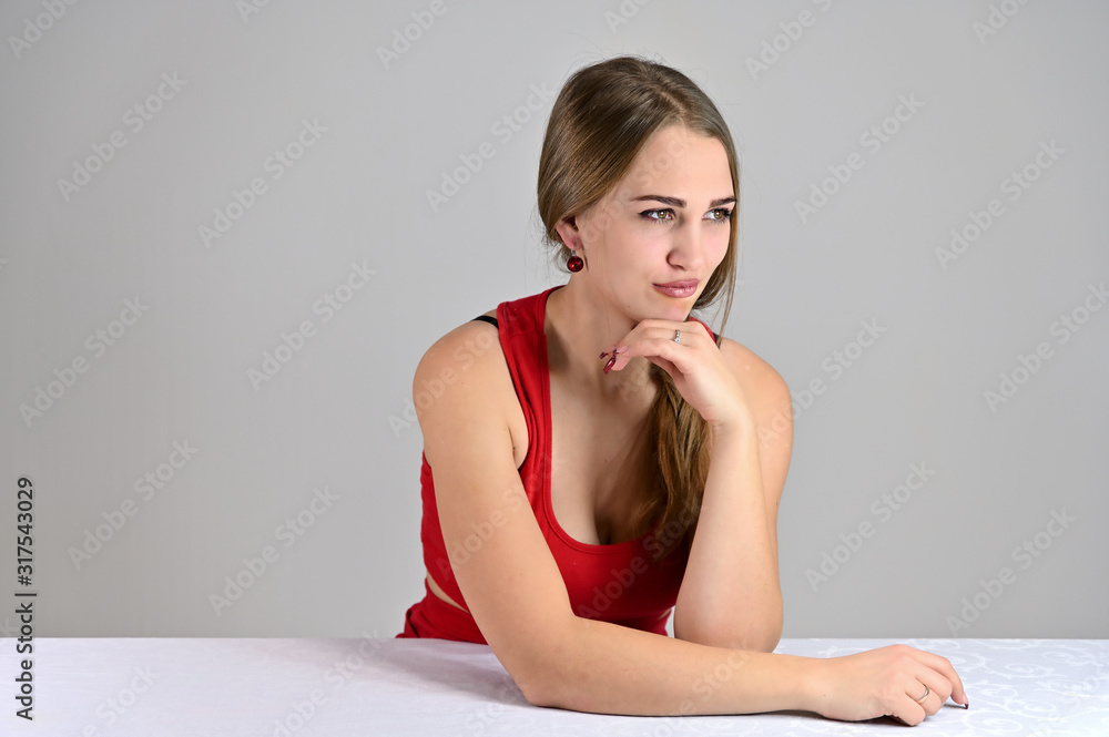 Universal concept female portrait on a white background. Horizontal photo of a pretty smiling girl with long hair and great makeup sitting at a white table in the studio. Universal concept female portrait on a white background. Horizontal photo of a pretty smiling girl with long hair and great makeup sitting at a white table in the studio.
