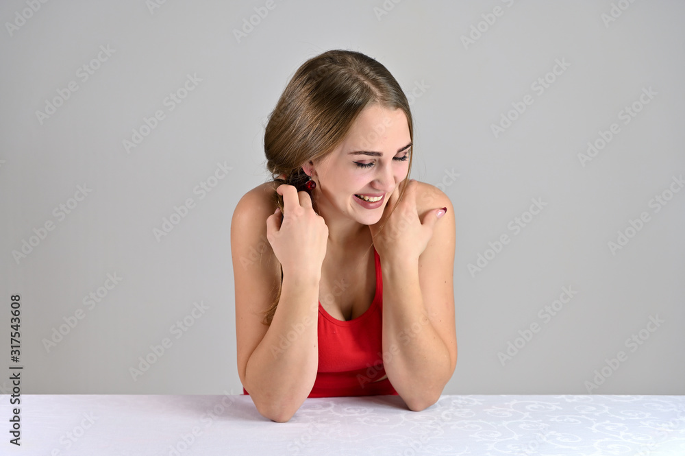 Horizontal photo of a pretty smiling girl with long hair and great makeup sitting at a white table in the studio. Universal concept female portrait on a white background. Horizontal photo of a pretty smiling girl with long hair and great makeup sitting at a white table in the studio. Universal concept female portrait on a white background.