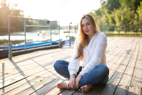 Beautiful girl sitting on wooden floor at sunset