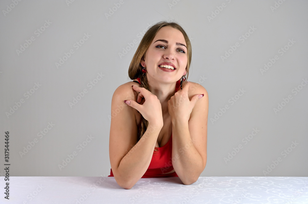 Horizontal photo of a pretty smiling girl with long hair and great makeup sitting at a white table in the studio. Universal concept female portrait on a white background. Horizontal photo of a pretty smiling girl with long hair and great makeup sitting at a white table in the studio. Universal concept female portrait on a white background.