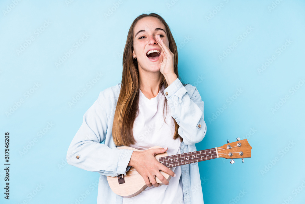 Fototapeta premium Young caucasian woman holding a ukelele isolated shouting excited to front.