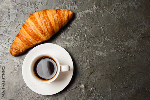 Coffee in white cup and croissant on a dark concrete background, top view, flat lay. Concept for breakfast, coffee break or business lunch. There is a place for text on the right