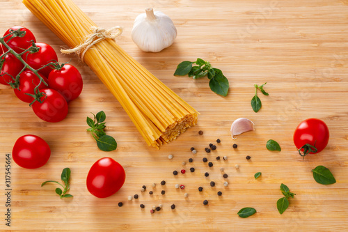Spaghetti raw, tomatoes, garlic, basil, spices on a wooden table.