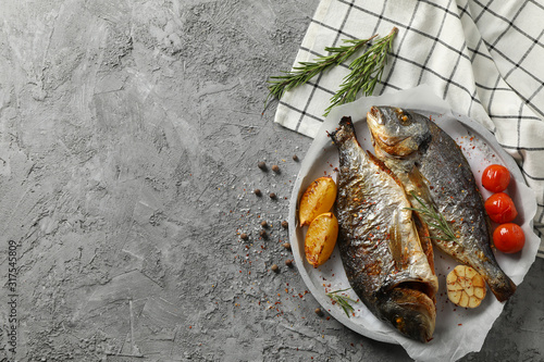 Plate with baked Dorado on garnished grey background, top view