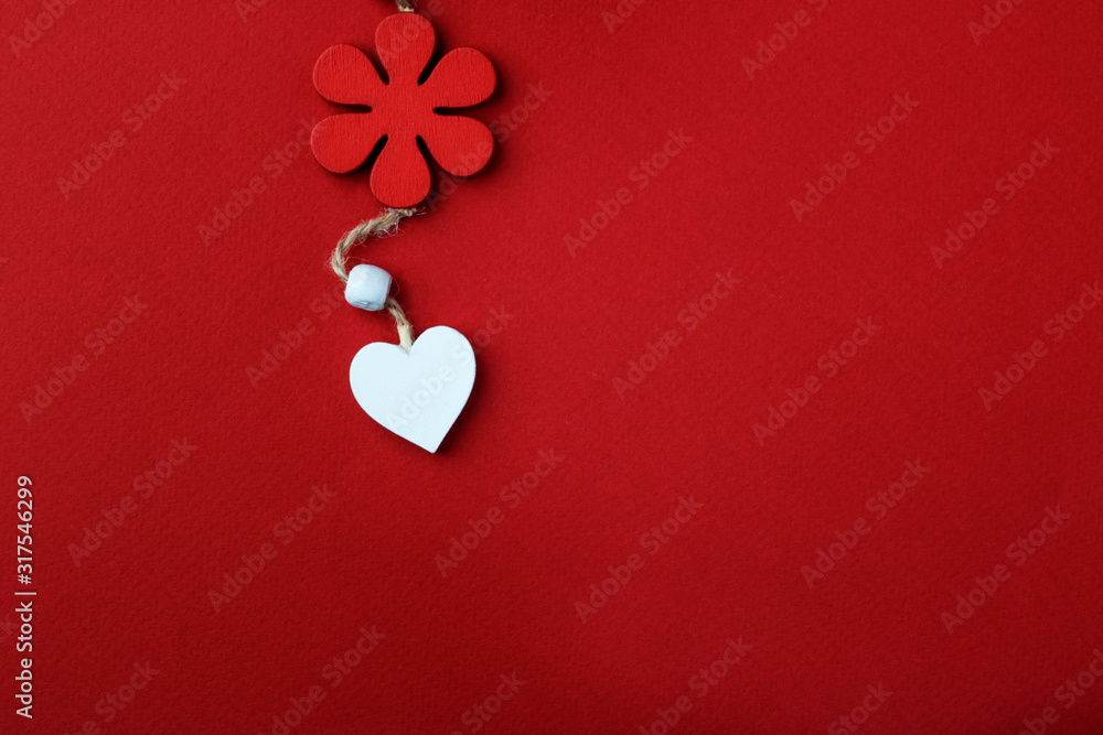Composition background for Valentine's Day. A white heart made of wood hangs on a natural thread under a red flower, on a red background. Copy space