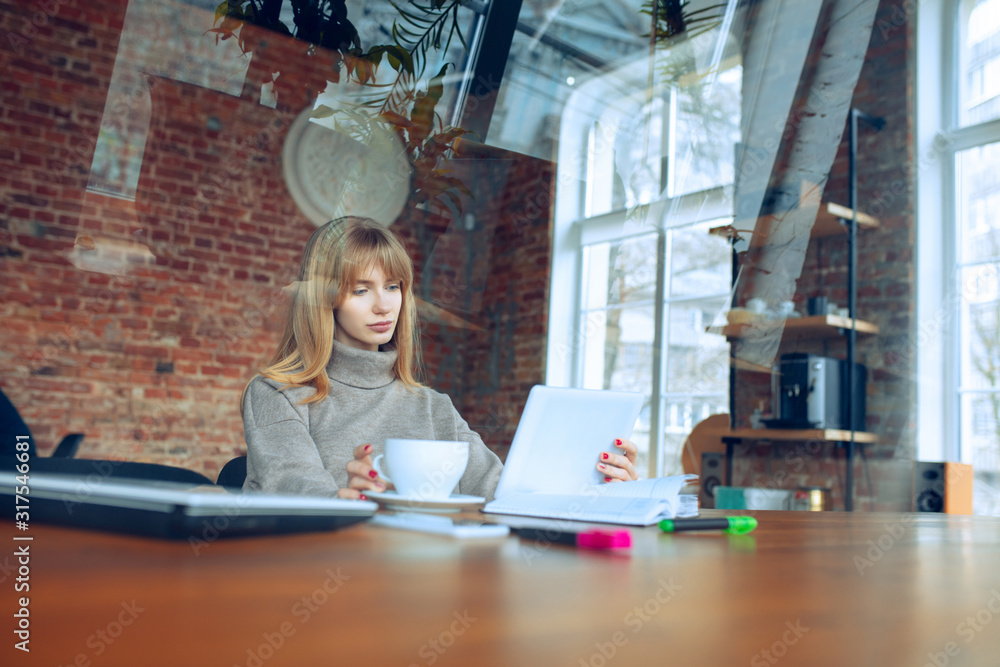 Beautiful caucasian business lady working in office with laptop. Young female model in co-working place makes notes, drinks coffee, performes tasks. Concept of business, finance, freelance, open space Beautiful caucasian business lady working in office with laptop. Young female model in co-working place makes notes, drinks coffee, performes tasks. Concept of business, finance, freelance, open space