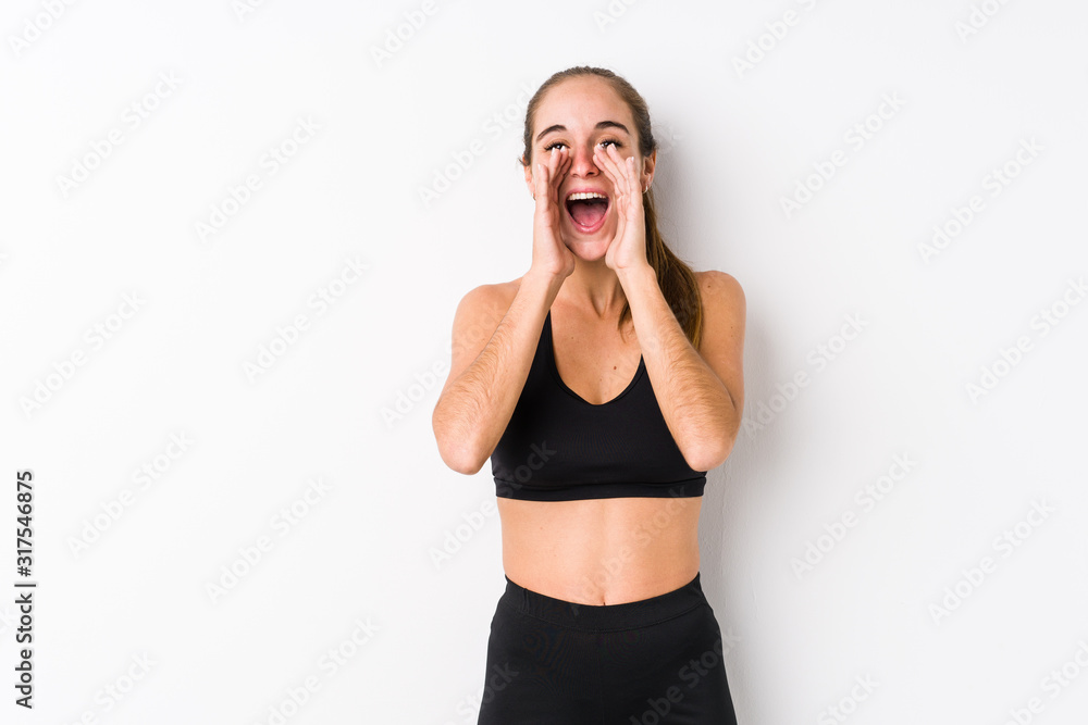 Young caucasian fitness woman posing in a white background shouting excited to front. Young caucasian fitness woman posing in a white background shouting excited to front.