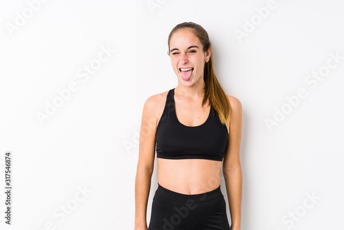 Young caucasian fitness woman posing in a white background funny and friendly sticking out tongue. © Asier
