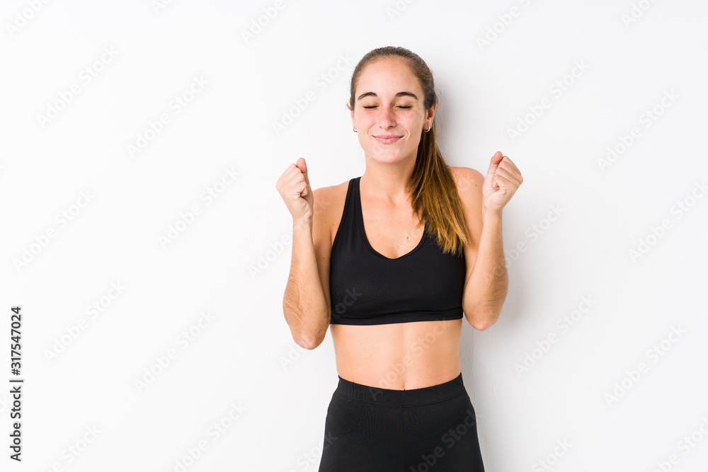 Young caucasian fitness woman posing in a white background raising fist, feeling happy and successful. Victory concept. Young caucasian fitness woman posing in a white background raising fist, feeling happy and successful. Victory concept.