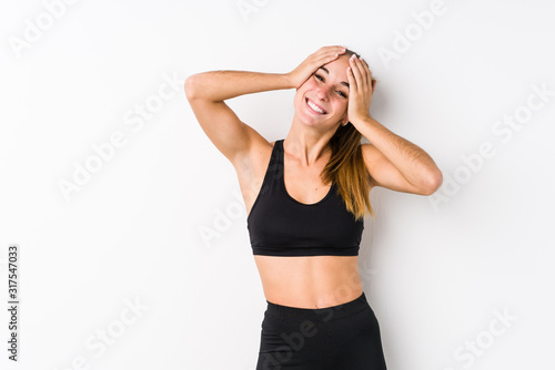Young caucasian fitness woman posing in a white background laughs joyfully keeping hands on head. Happiness concept. © Asier