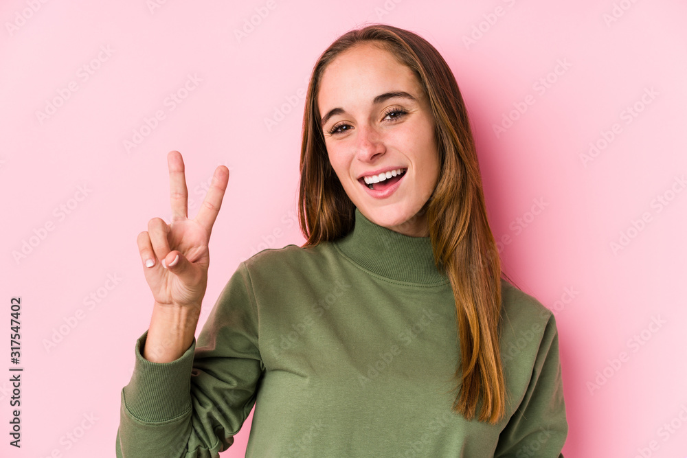 Young caucasian woman posing isolated joyful and carefree showing a peace symbol with fingers. Young caucasian woman posing isolated joyful and carefree showing a peace symbol with fingers.