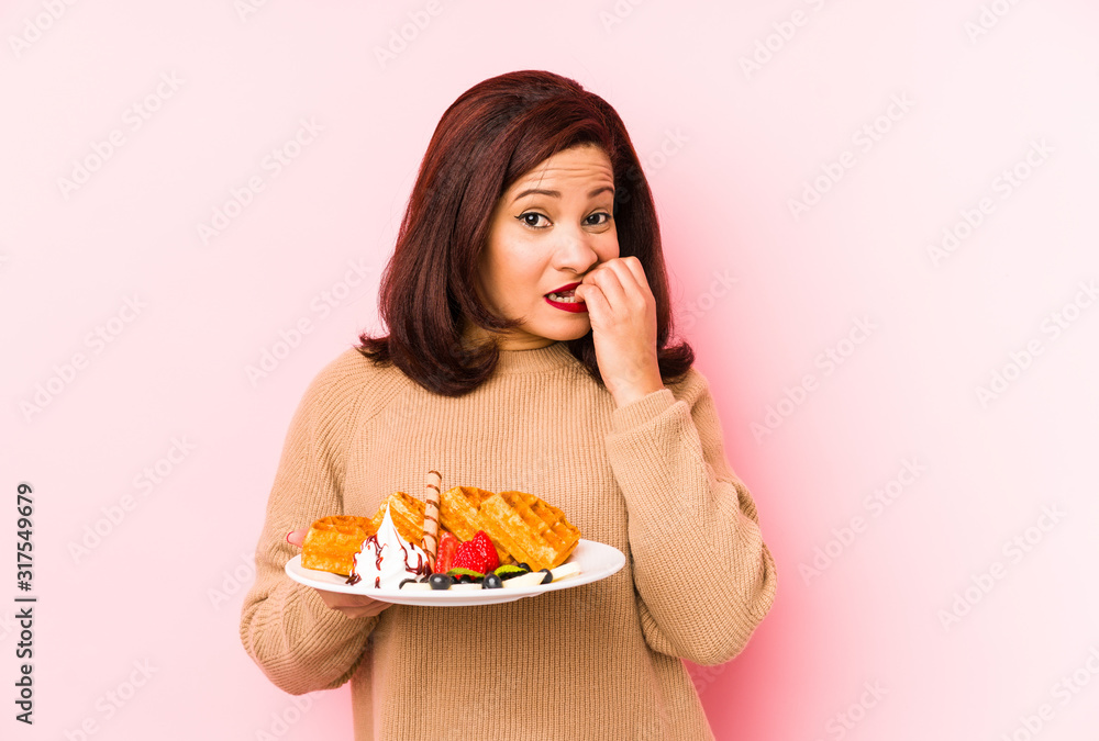 Middle age latin woman holding a waffle isolated biting fingernails, nervous and very anxious. Middle age latin woman holding a waffle isolated biting fingernails, nervous and very anxious.
