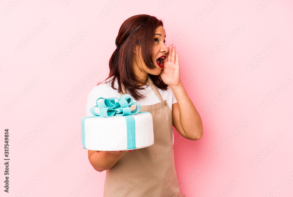 Middle age latin woman holding a cake isolated on a pink background shouting and holding palm near opened mouth. Middle age latin woman holding a cake isolated on a pink background shouting and holding palm near opened mouth.