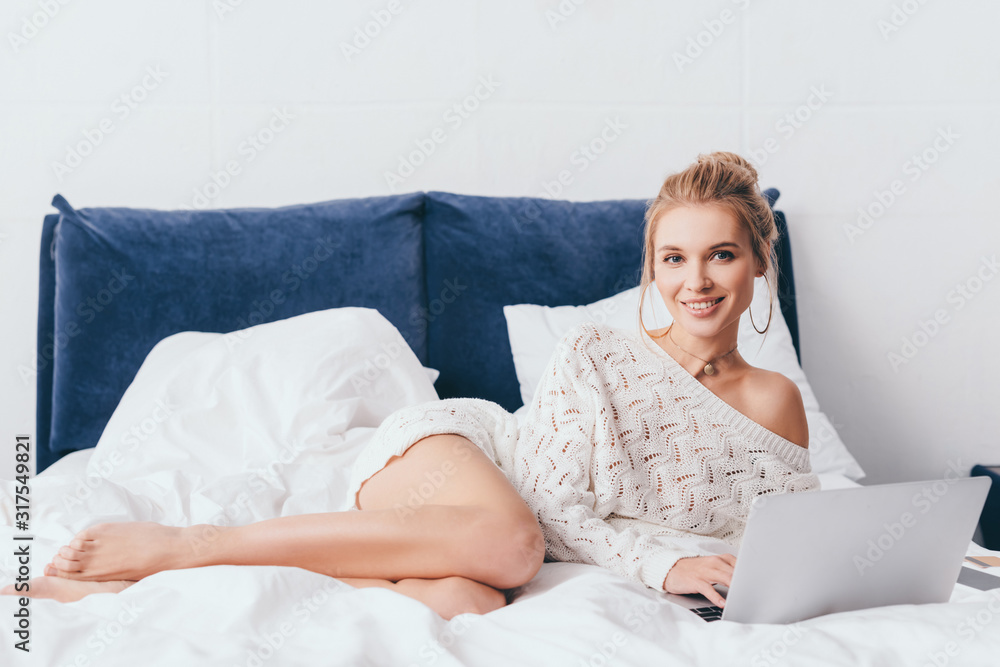 attractive cheerful woman using laptop on bed with sheets in morning attractive cheerful woman using laptop on bed with sheets in morning