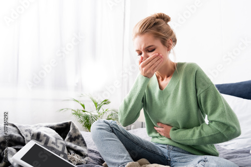 woman having nausea and sitting on bed with digital device photo