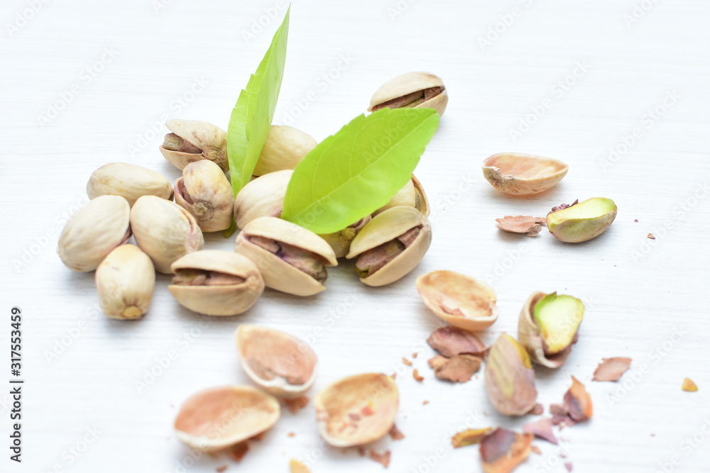  Pistachios on the white wooden background, accompanied by green leaf