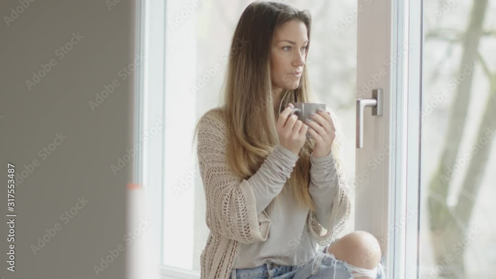 beautiful brunette drinking coffee and looking through a window in her new home. beautiful brunette drinking coffee and looking through a window in her new home.