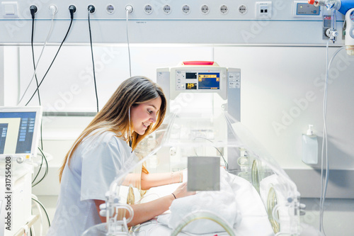 Nurse gently touching fragile newborn in neonatal incubator photo