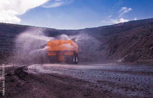 Heavy truck pours the road with water in the iron ore quarry. Dust removal, protection of the environment. Irrigation of the road from dust. The World’s Largest Sprinkler Truck