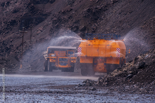 Heavy truck pours the road with water in the iron ore quarry. Dust removal, protection of the environment. Irrigation of the road from dust. The World’s Largest Sprinkler Truck