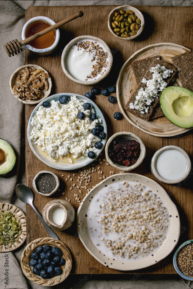 Healthy breakfast. Variety of breakfast dishes wheat, yogurt, kefir, cottage cheese, avocado, rye bread, seeds, nuts and berries assortment in ceramic bowls. Wooden and textile background. Flat lay Healthy breakfast. Variety of breakfast dishes wheat, yogurt, kefir, cottage cheese, avocado, rye bread, seeds, nuts and berries assortment in ceramic bowls. Wooden and textile background. Flat lay