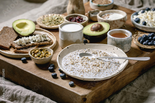 Healthy breakfast. Variety of breakfast dishes sprouted wheat, yogurt, kefir, cottage cheese, avocado, rye bread, seeds, nuts and berries assortment in ceramic bowls over wooden serving board.
