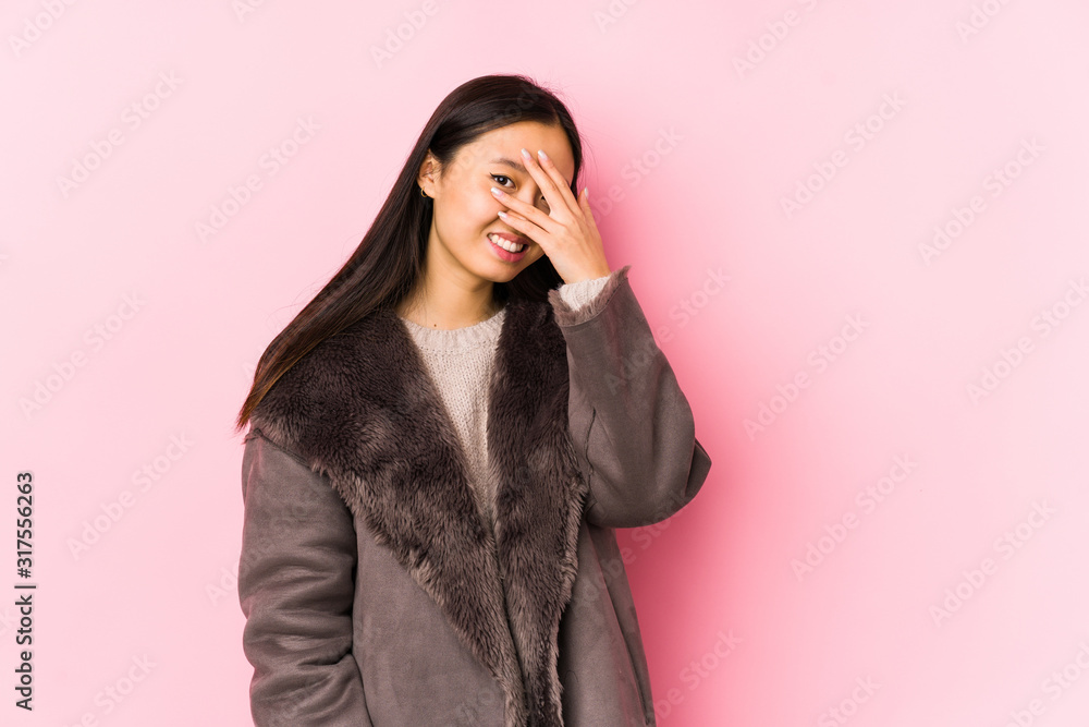 Young chinese woman wearing a coat isolated blink at the camera through fingers, embarrassed covering face. Young chinese woman wearing a coat isolated blink at the camera through fingers, embarrassed covering face.