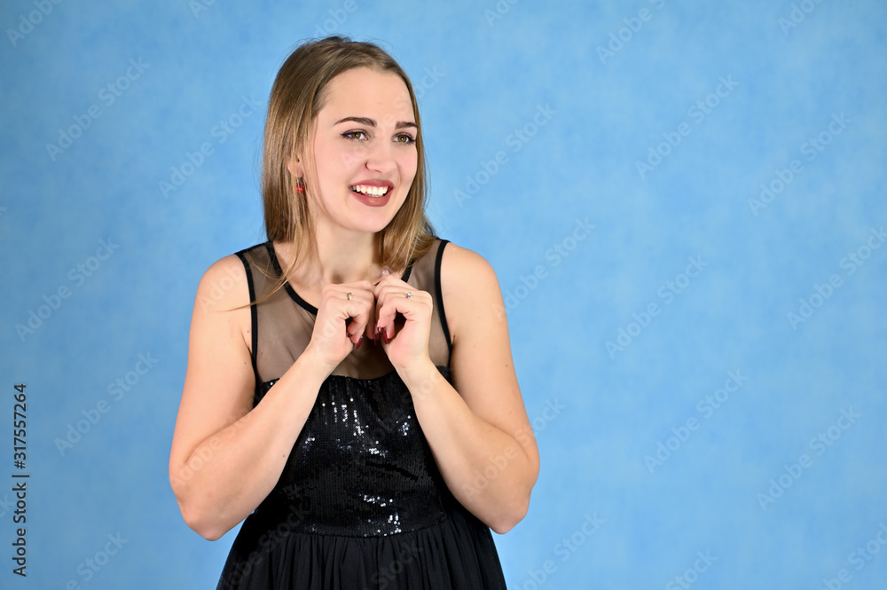 Fototapeta premium Universal concept horizontal portrait of a woman on a blue background. A photo of a pretty smiling girl with long hair and excellent make-up in a black dress stands in different poses.