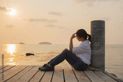 Beautiful woman sitting Alone with loneliness At the wooden bridge by the sea During sunset