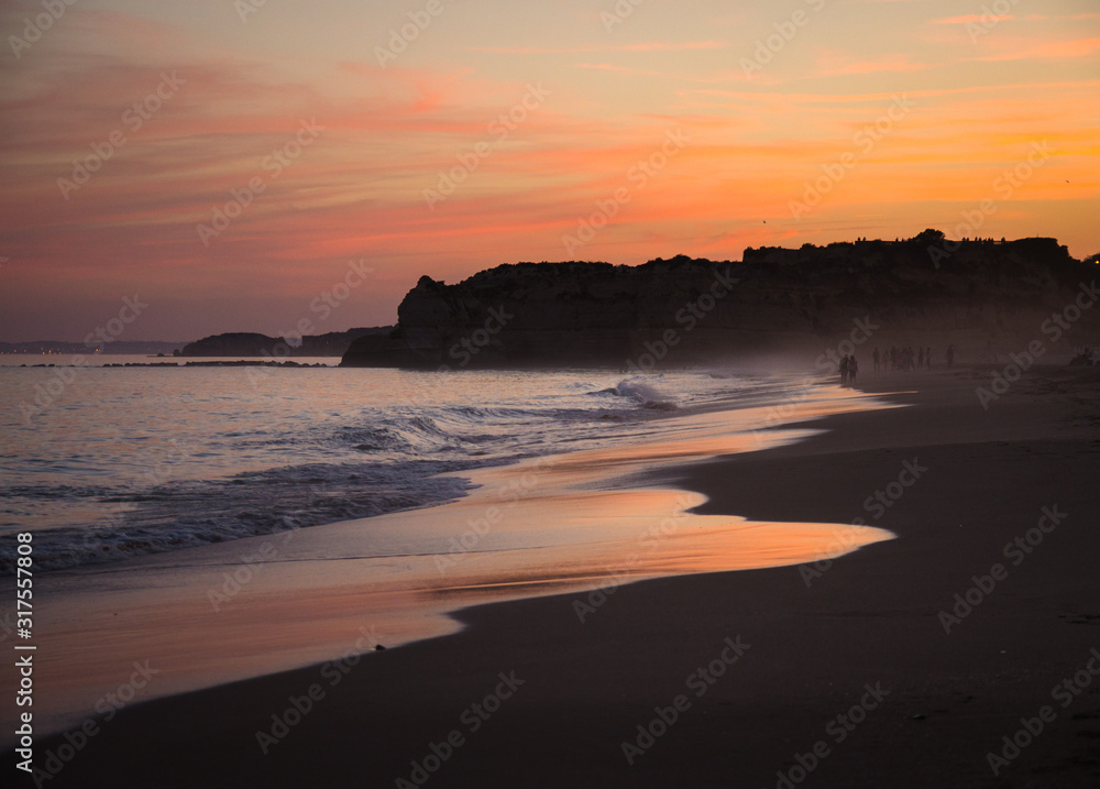 Portugal, Algarve, The best beaches of Portimao, evening view of the cliff in Algarve, red sky over the cliff, landscape of sea coast, people on the beach at sunset, evening haze on the ocean beach