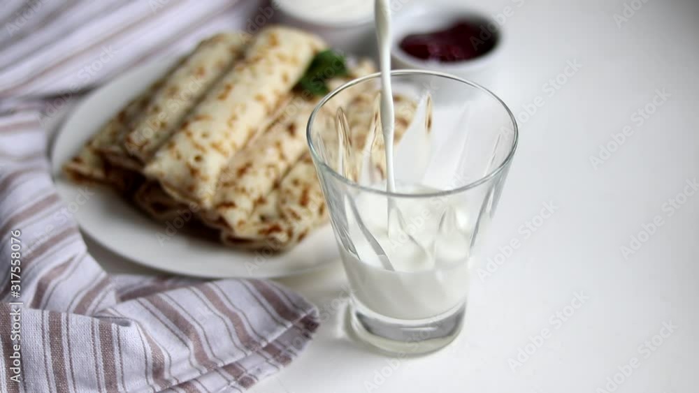 Breakfast with pancakes and milk. Milk is poured into a transparent glass. In the background is a plate and a fresh napkin. Copy space. Breakfast with pancakes and milk. Milk is poured into a transparent glass. In the background is a plate and a fresh napkin. Copy space.