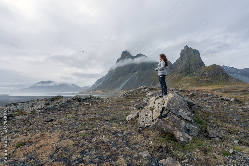 Beautiful Girl stands on a rock looking towards the sea on Hvalnes Peninsula in the southcoast of Iceland. Eystrahorn in the background.