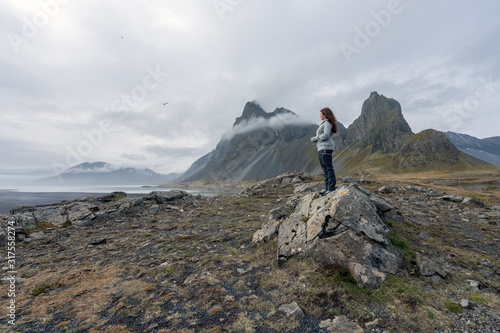 Beautiful Girl stands on a rock looking towards the sea on Hvalnes Peninsula in the southcoast of Iceland. Eystrahorn in the background.