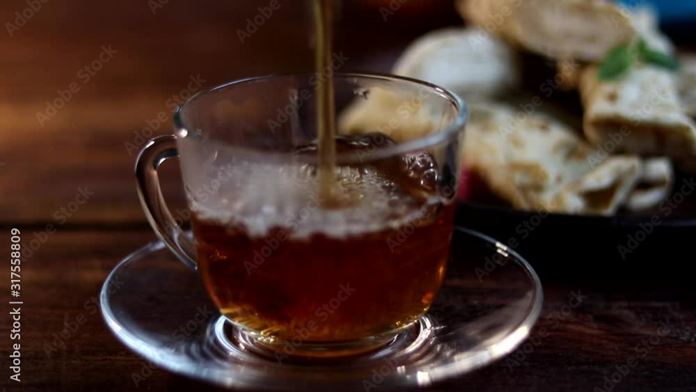 Breakfast with pancakes and tea. Hot tea is poured into a transparent cup. On a wooden background. In the background is a plate and a light napkin. Breakfast with pancakes and tea. Hot tea is poured into a transparent cup. On a wooden background. In the background is a plate and a light napkin.